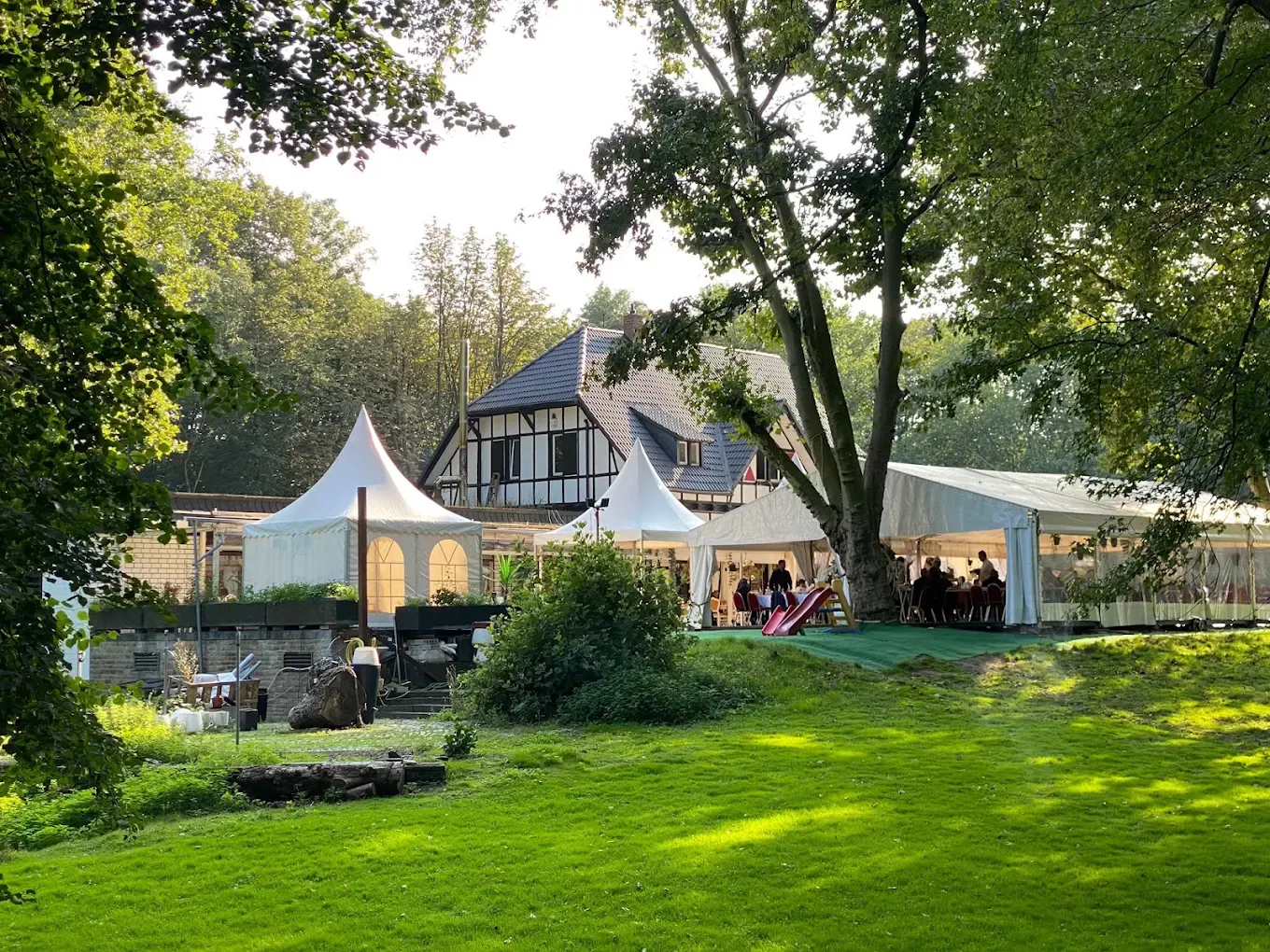 Garten mit Zelten und dem Fachwerkhaus des Restaurants im Abendlicht